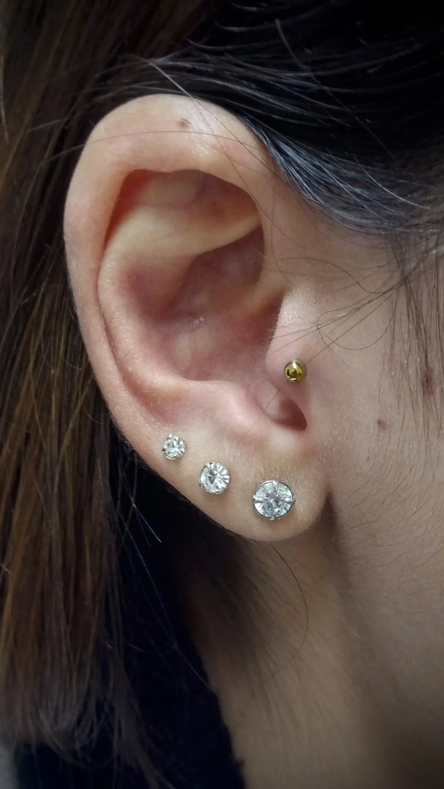 Close da orelha de uma mulher com três brincos.