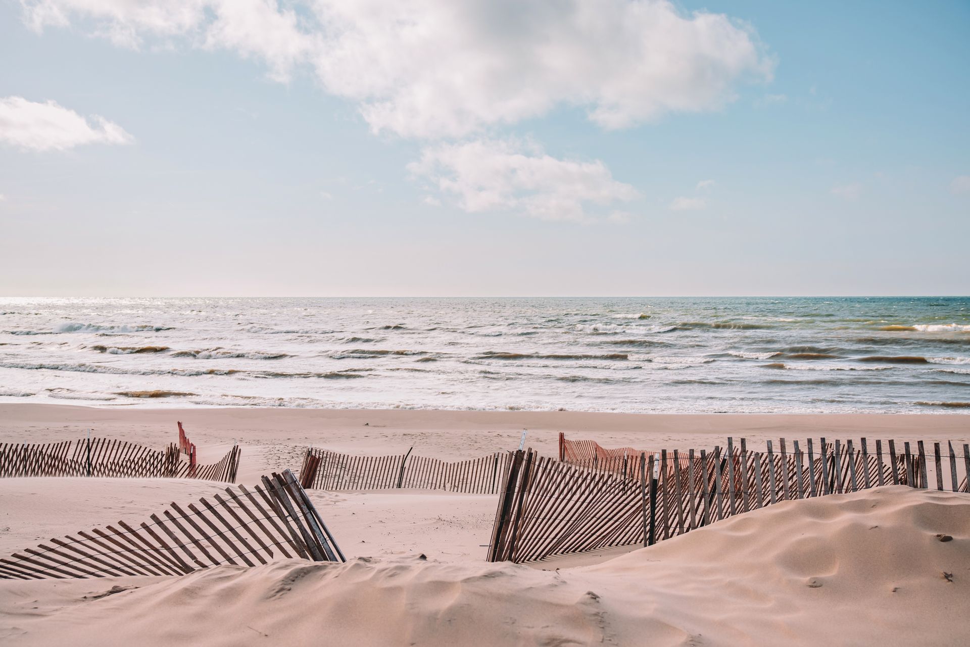 Sandy beach with weathered wooden fences, ocean, and cloudy sky.