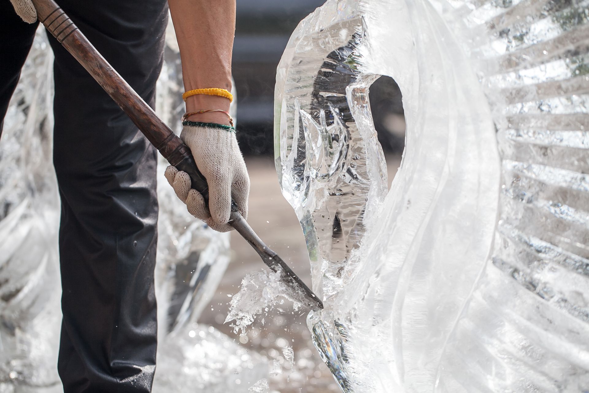Person using a chisel to sculpt ice outdoors. Water splashing as the ice is being carved.