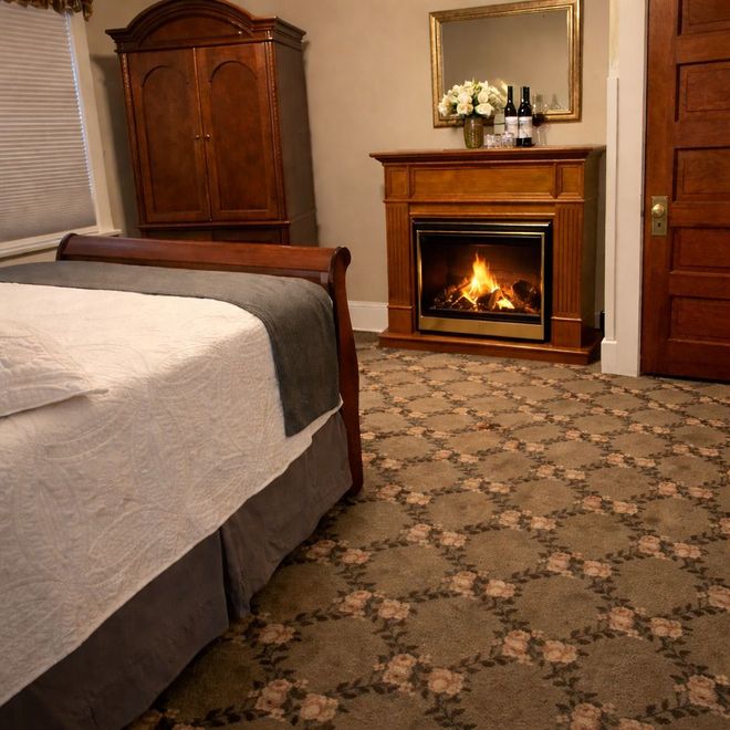 A bed with white bedding, headboard, and decorative spread, in a bedroom with artwork and a lamp.