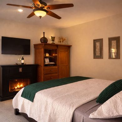 A bed with white bedding, headboard, and decorative spread, in a bedroom with artwork and a lamp.