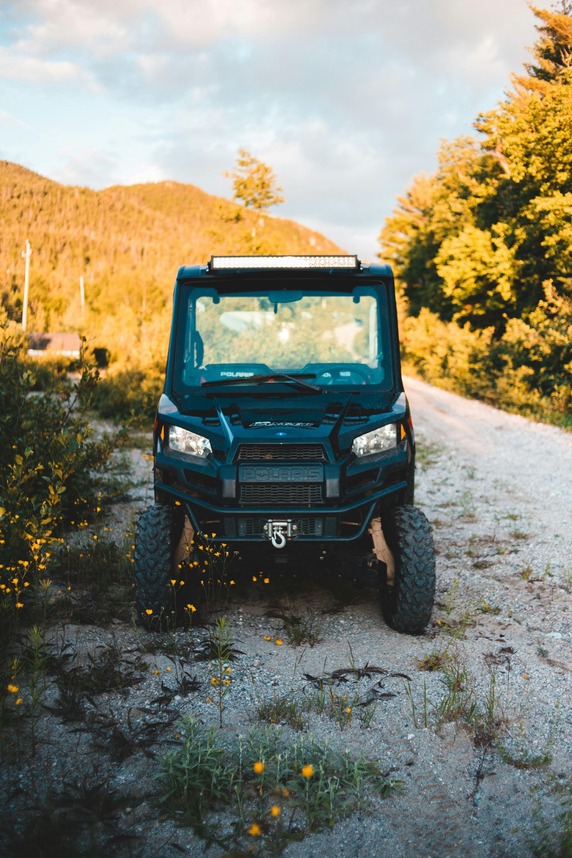 Black off-road vehicle on a gravel road, parked in a forest setting with a mountain in the background.