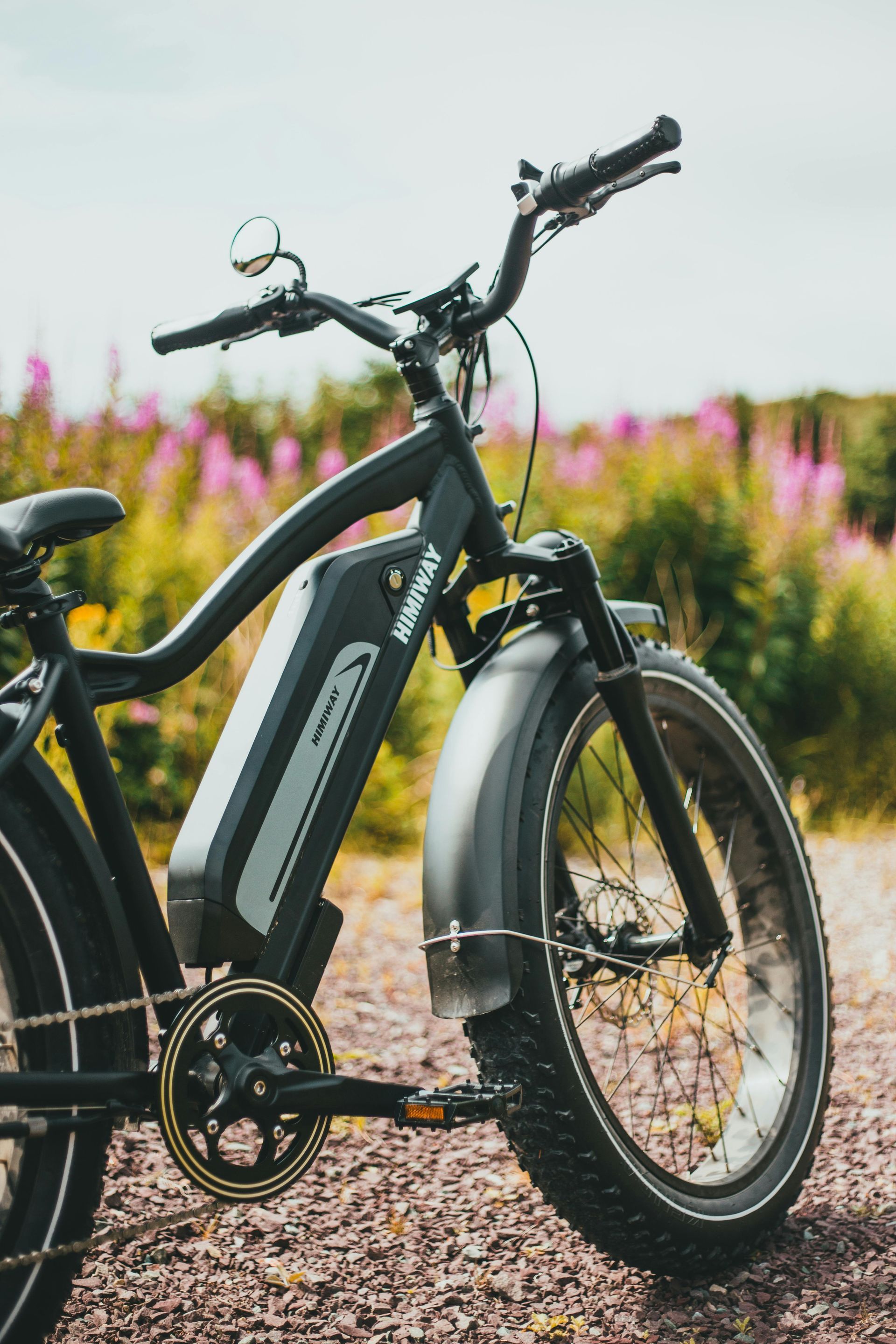 Black electric bicycle with a battery pack, on a gravel path, wildflowers in the background.