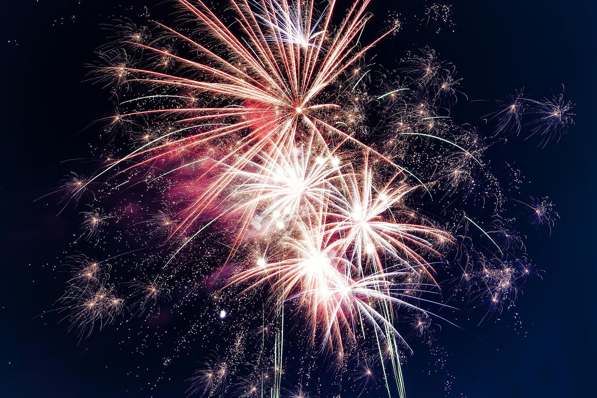 Fireworks bursting against a dark blue sky, displaying red and white explosions.