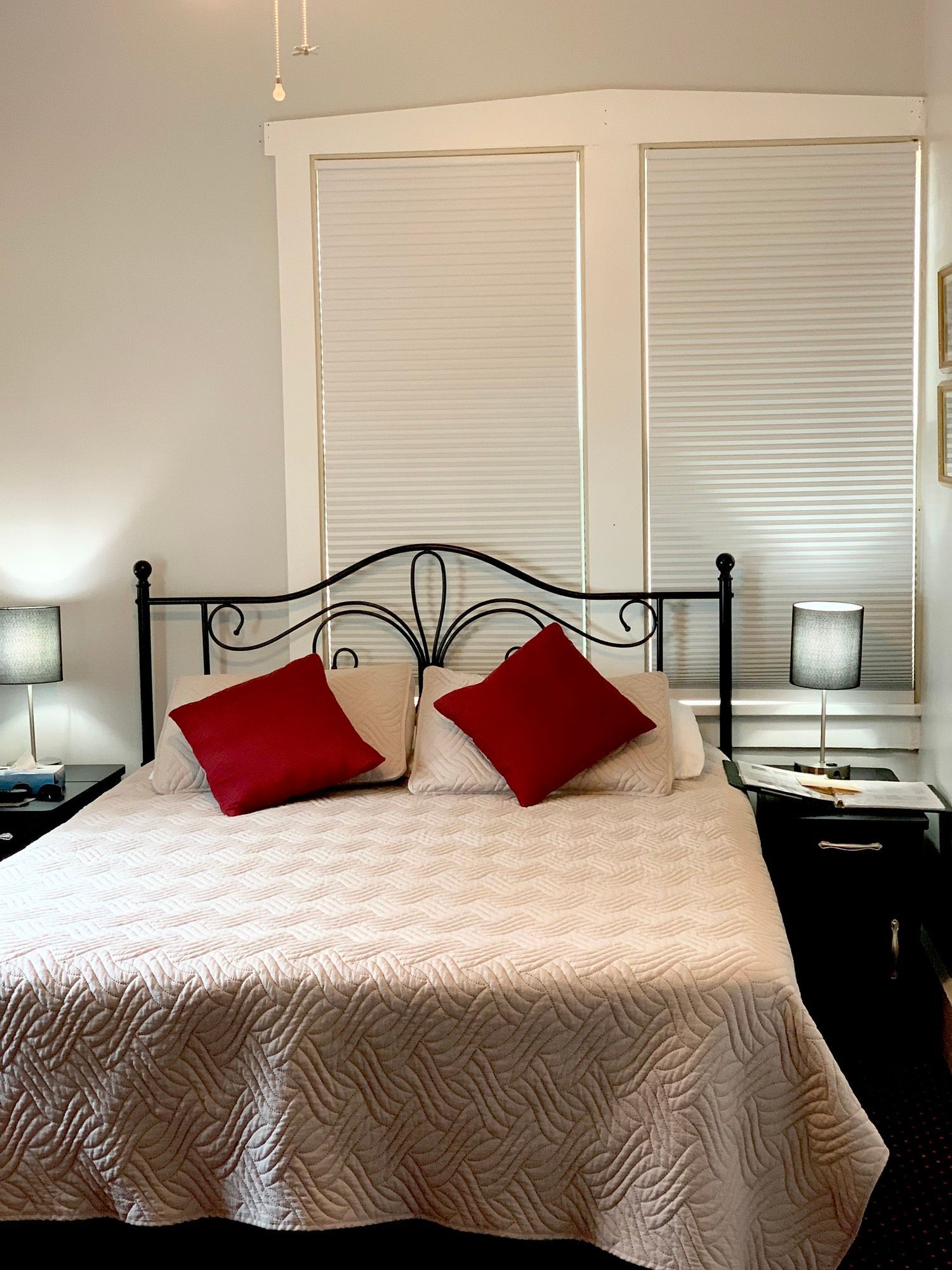 Bedroom with a bed, two red pillows, white bedspread, two nightstands, two lamps, and a window.