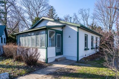 White cottage with green trim, screened porch, small concrete steps, and bare trees.