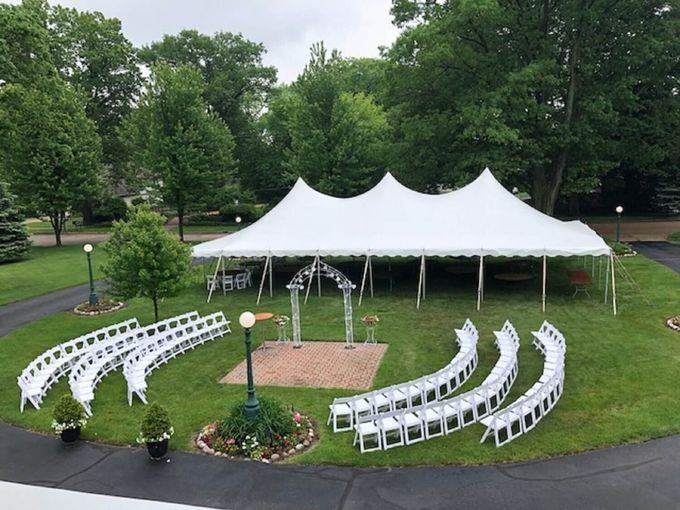 Wedding ceremony setup outdoors with white tent, rows of chairs, and arch.