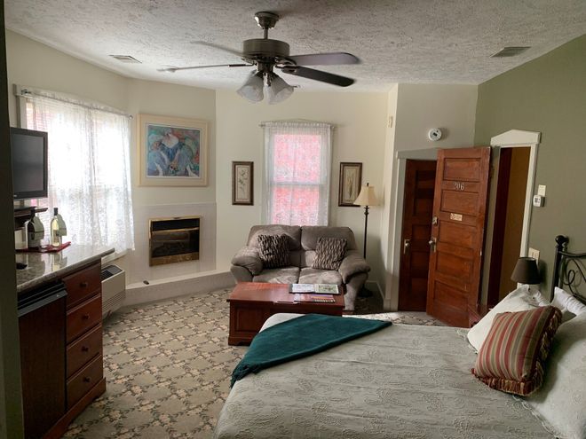 Cozy hotel room with bed, sofa, fireplace, and window. Brown furniture, patterned carpet, and green accents.