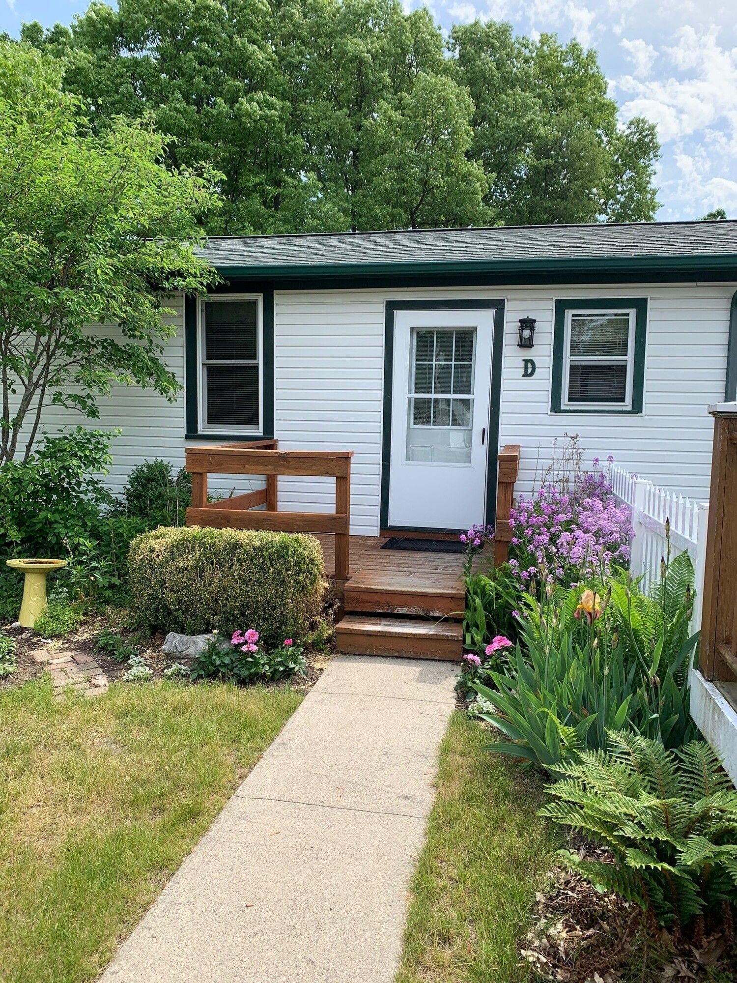 White cottage with green trim and a small wooden porch surrounded by a garden.