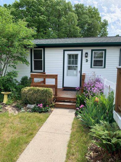 White cottage with green trim and a small wooden porch surrounded by a garden.