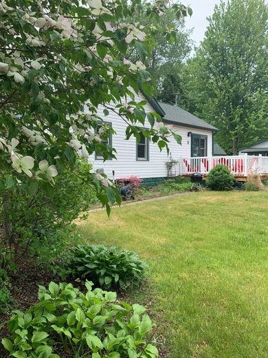 White house with a small porch and blooming tree in front. Green grass and garden in the yard.