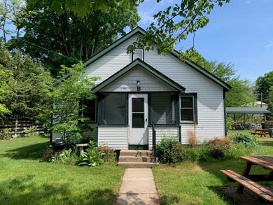 White cottage with green trim, screened porch, and concrete path leading to the door.