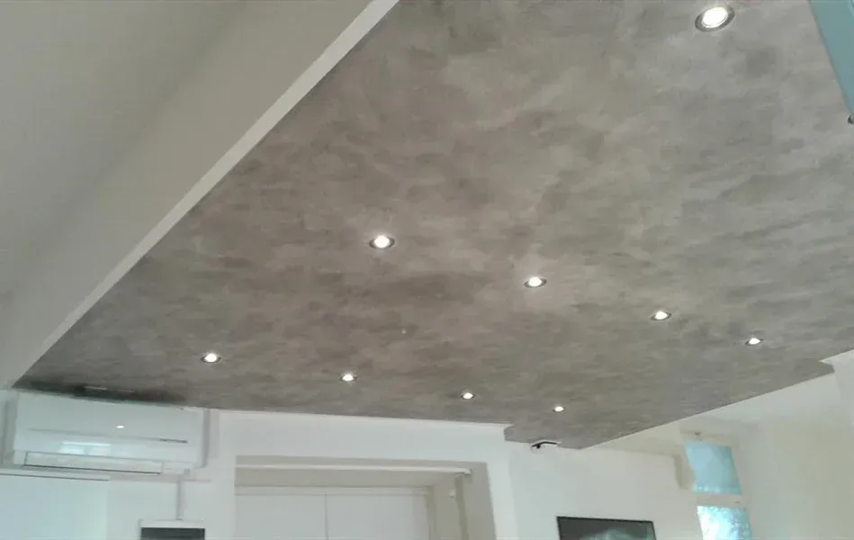 Soffitto grigio testurizzato con luci da incasso, sopra una stanza bianca con aria condizionata.