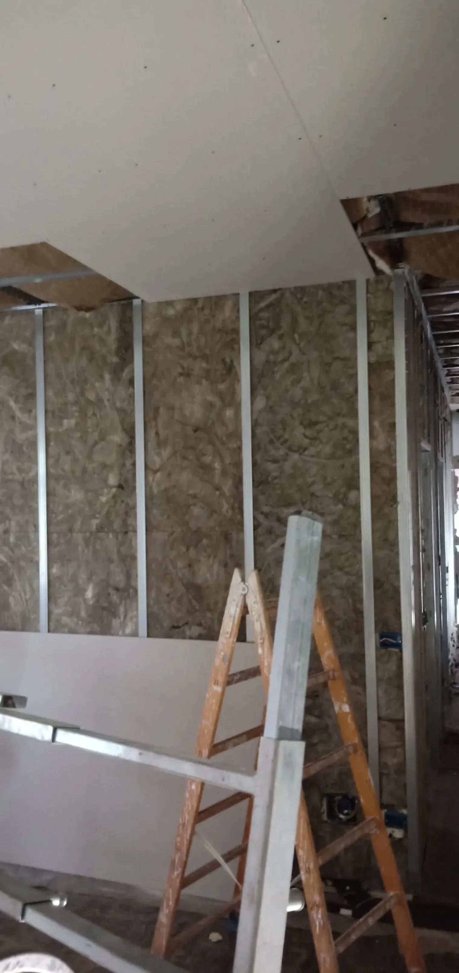 Costruzione interna che mostra l'isolamento tra i montanti metallici; cartongesso parzialmente installato; scale presenti.