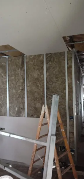 Costruzione interna che mostra l'isolamento tra i montanti metallici; cartongesso parzialmente installato; scale presenti.