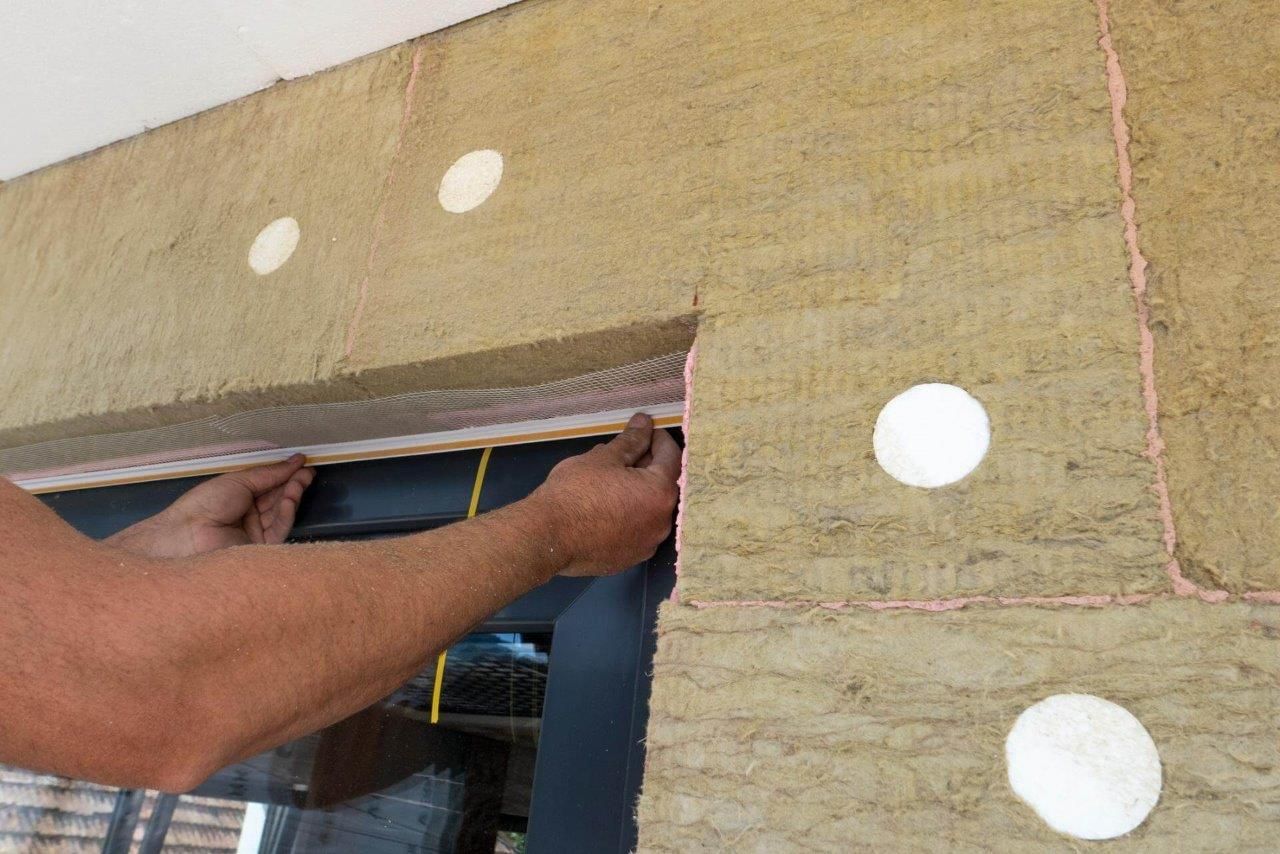 Persona che installa del nastro adesivo nero attorno al telaio di una finestra con isolamento, cappucci circolari bianchi.