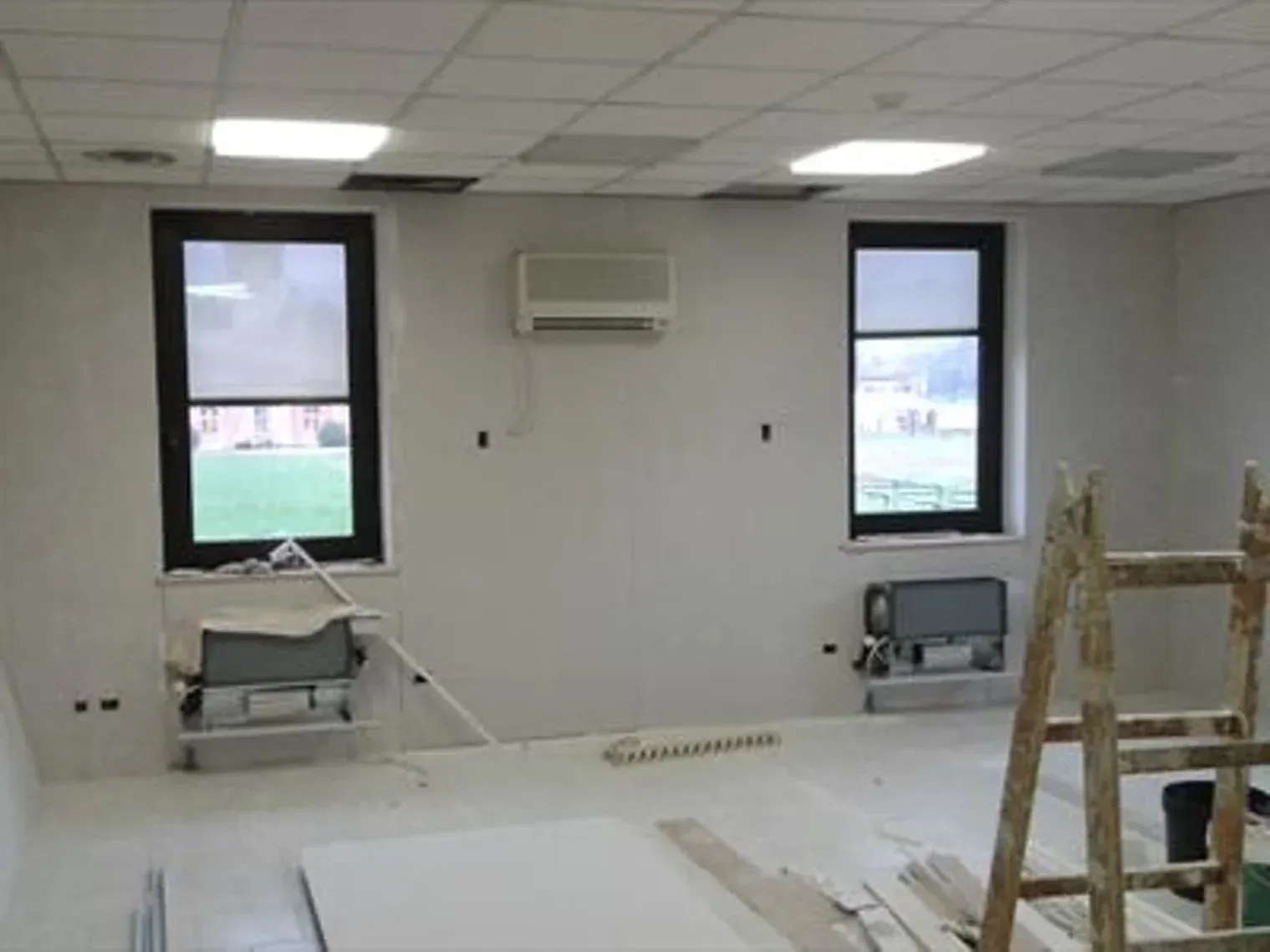 Stanza vuota, con pareti bianche, due finestre, aria condizionata e materiali da costruzione.