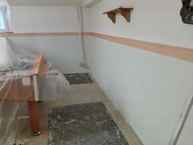 Stanza nel seminterrato con pareti bianche, finiture color cuoio, tavolo coperto e tappetini scuri.