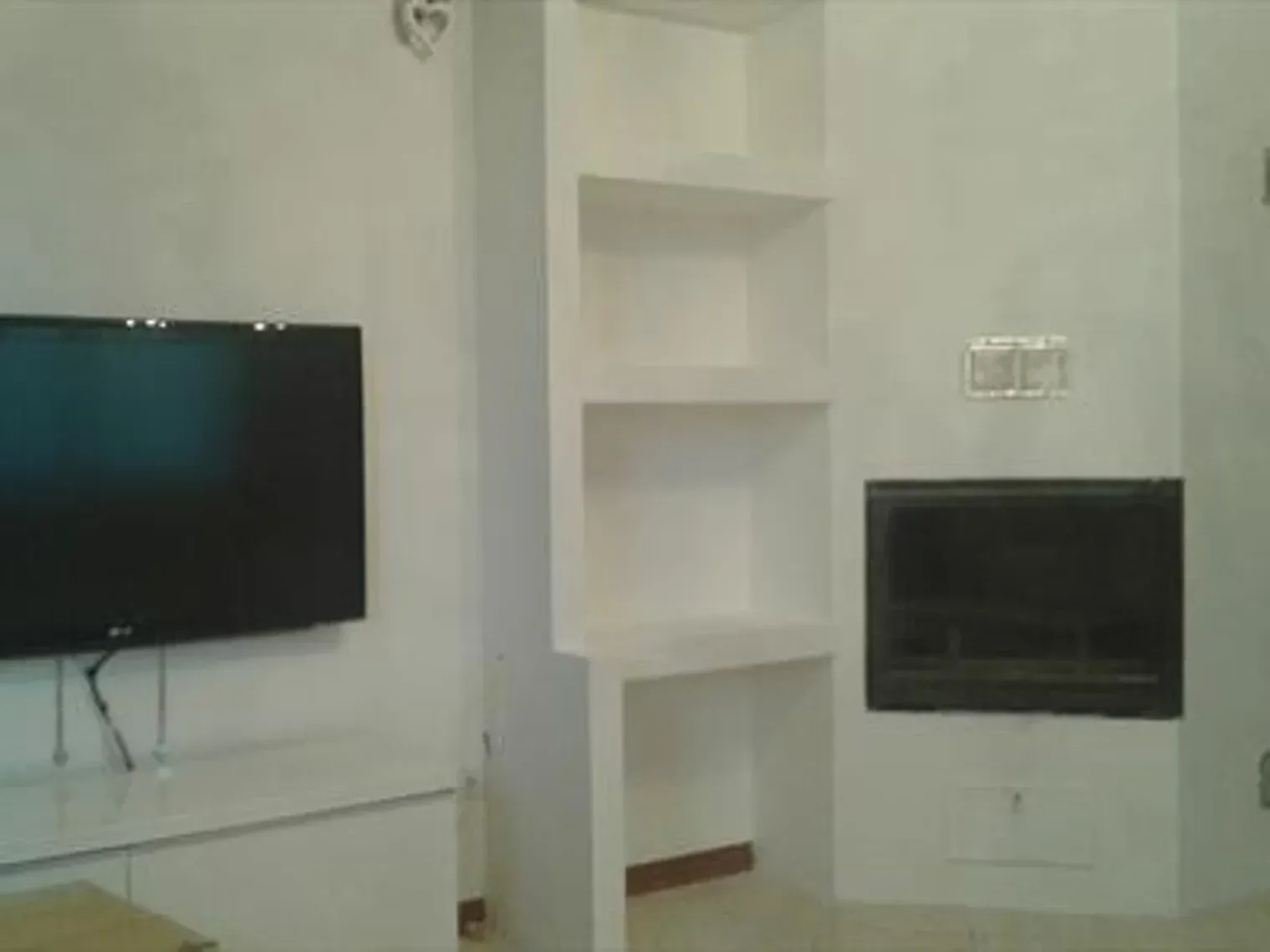 Mensole bianche integrate e un camino fiancheggiano una TV a schermo piatto su una parete bianca.