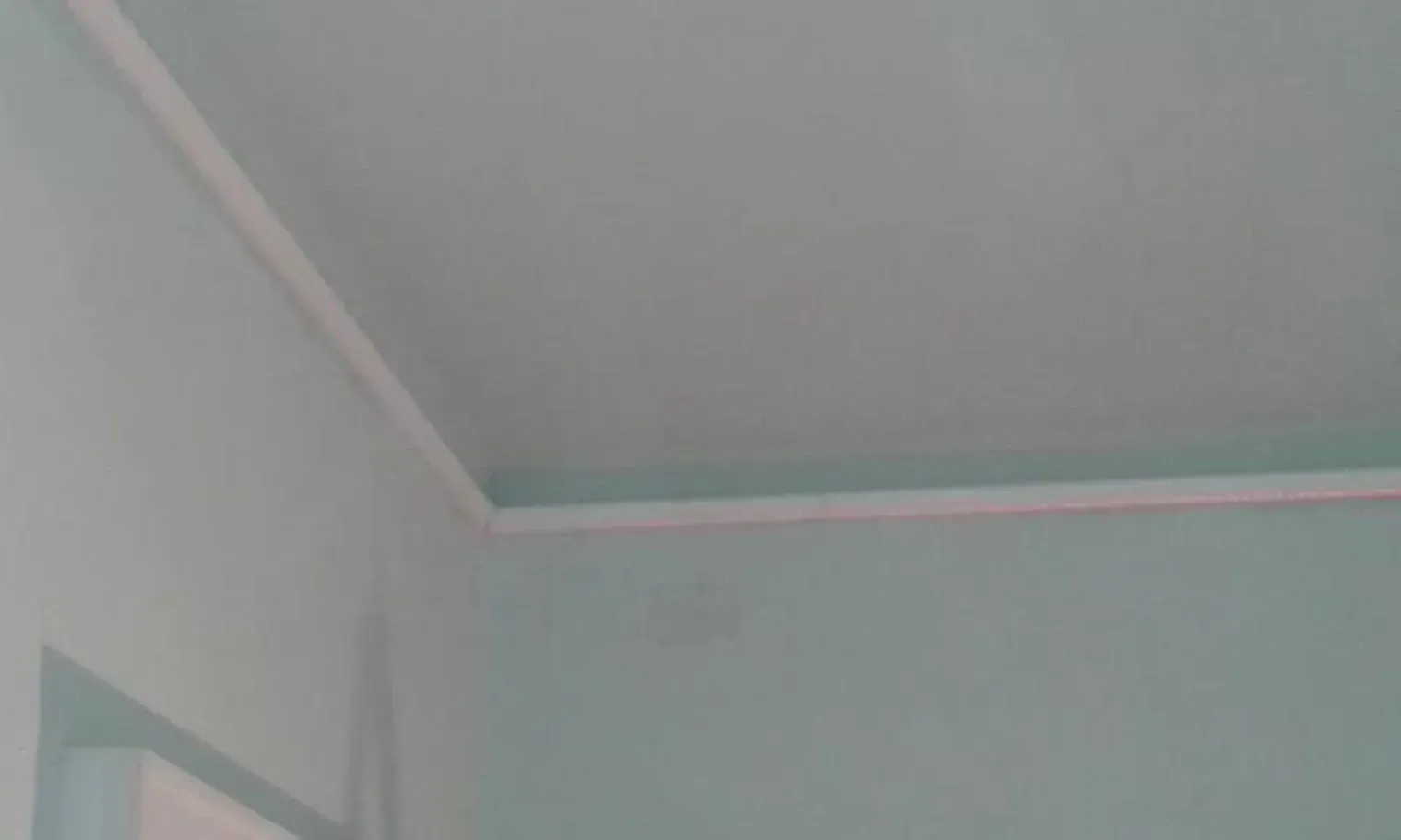 Angolo di una stanza con pareti azzurre e una modanatura bianca lungo il soffitto.