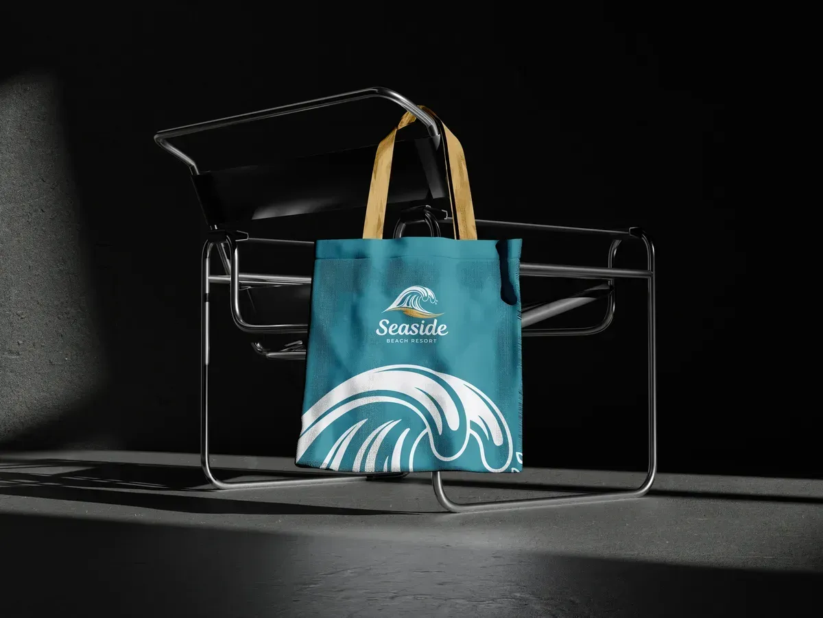 Teal Seaside tote bag with wave graphic on a chrome chair, dark background.
