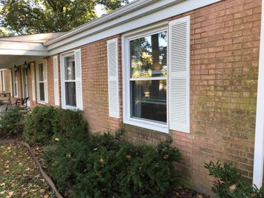 Brick house exterior with white shutters, windows, and shrubs along the front