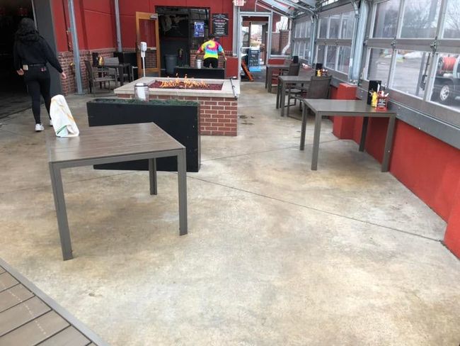 Covered outdoor seating area with tables and benches beside a red building, one person walking away