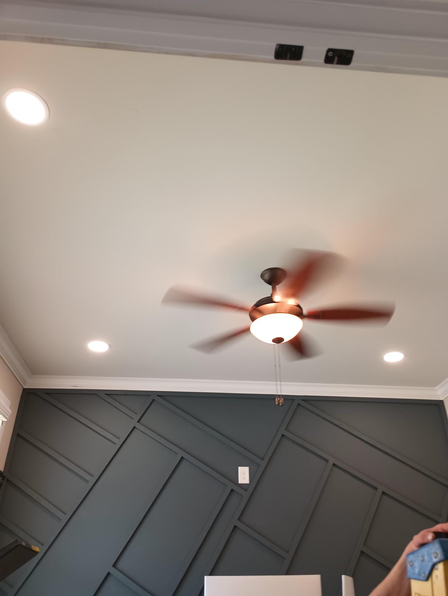 Ceiling fan and recessed lights in a room with a dark geometric accent wall.