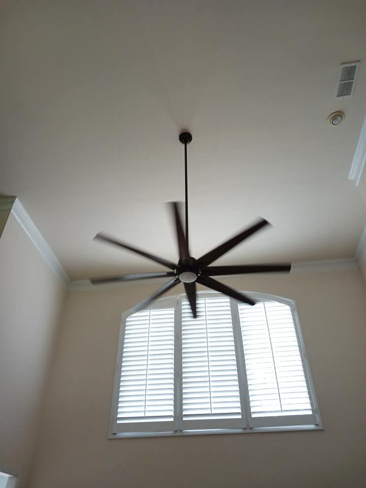 Ceiling fan with seven blades in a tall room with a shuttered window.
