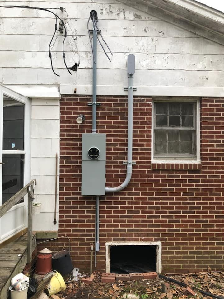 Electrical meter box mounted on a brick wall, with conduit and wiring extending upwards.