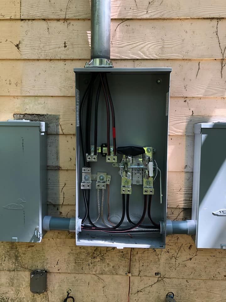 Electrical service panel on a building exterior with conduit and wiring visible.