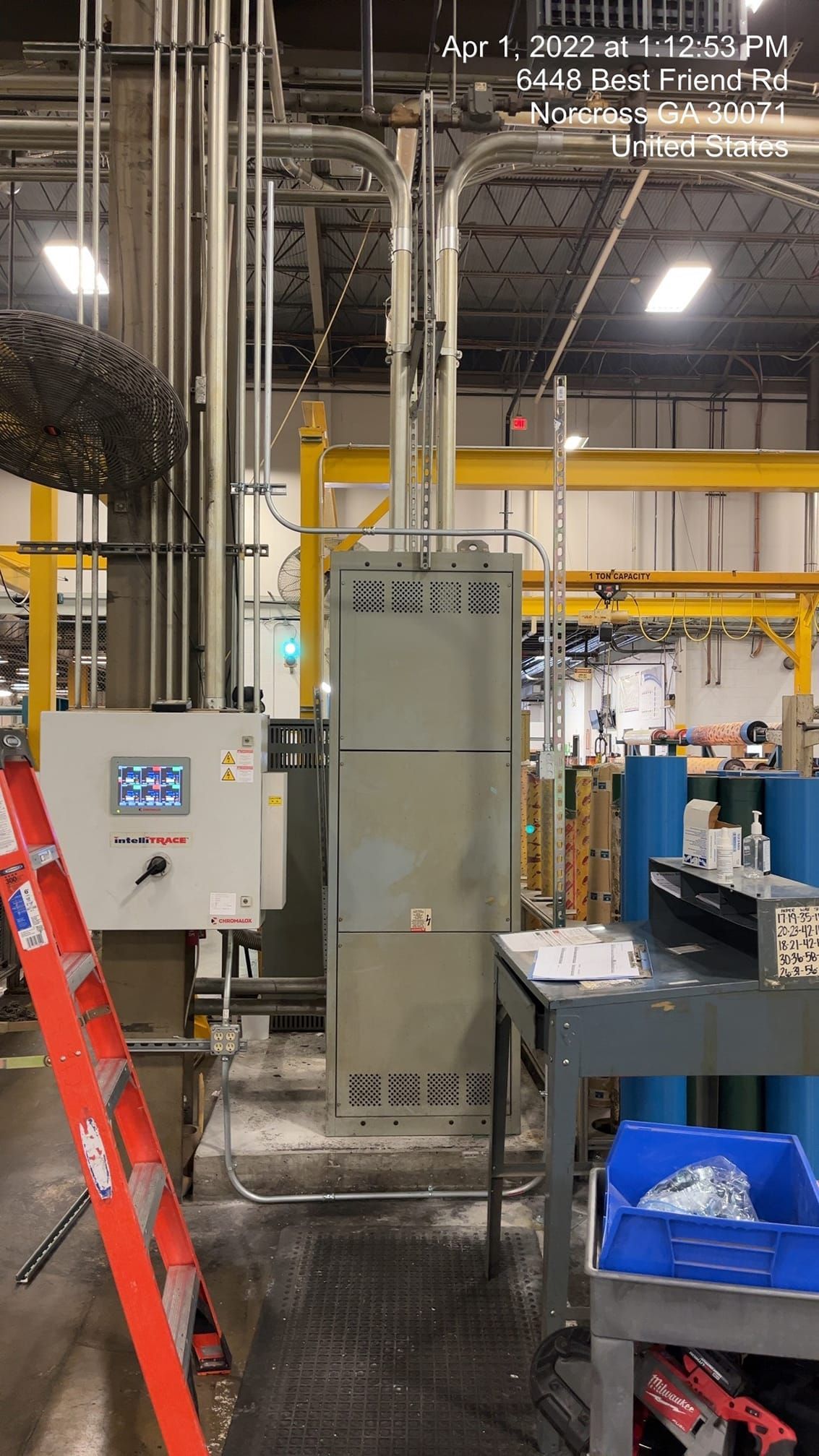 Gray industrial electrical panel with pipes and controls in a factory setting with a red ladder.