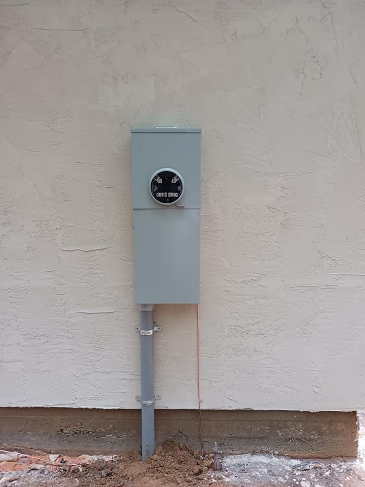 Gray electrical meter box on a stucco wall, with conduit running to the ground.