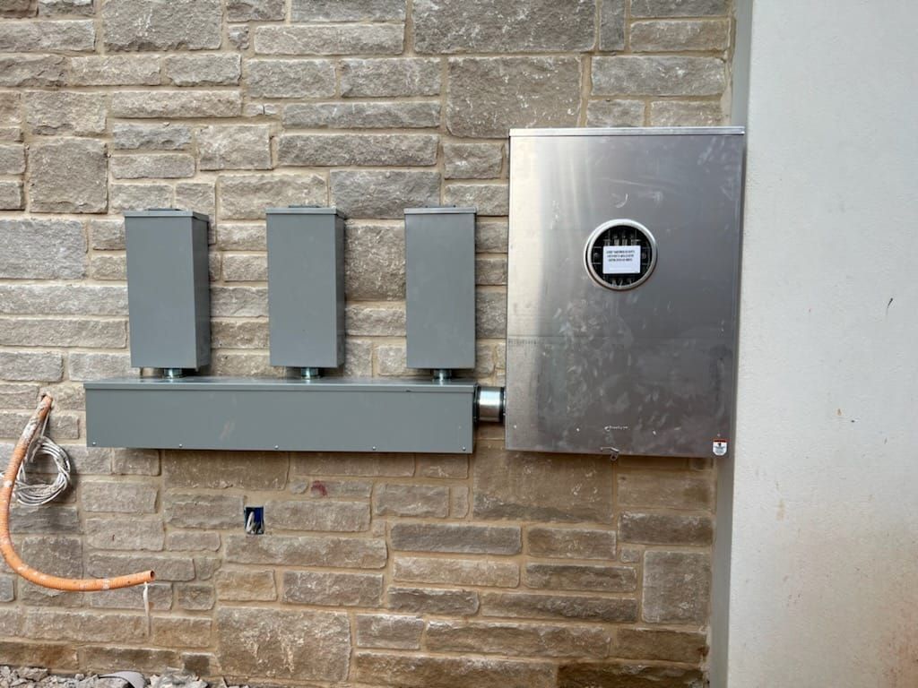 Gray electrical boxes and meter on a stone wall. Orange conduit and white pillar are visible.
