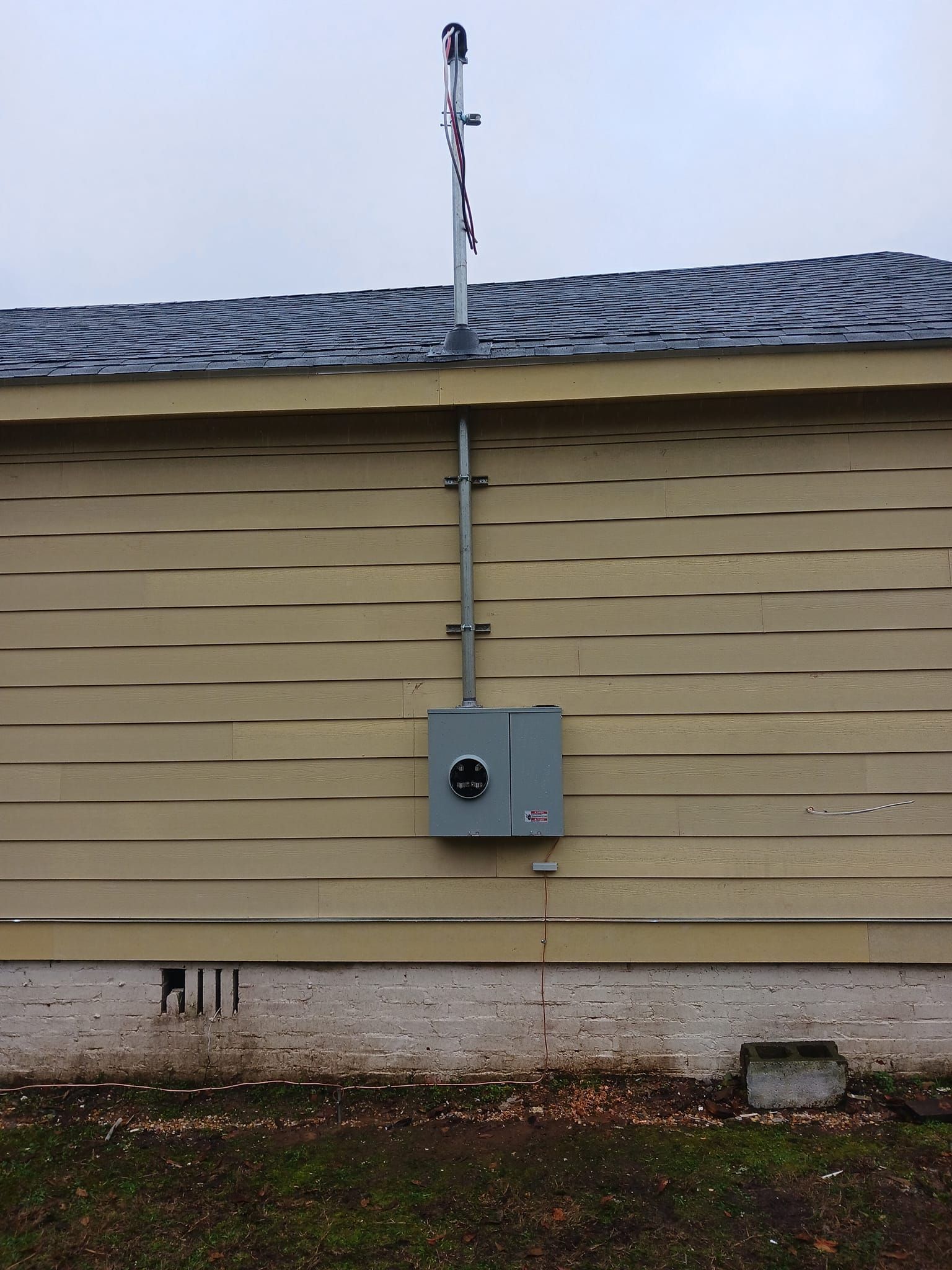 Electrical meter box and conduit on the side of a tan house, with an antenna attached.