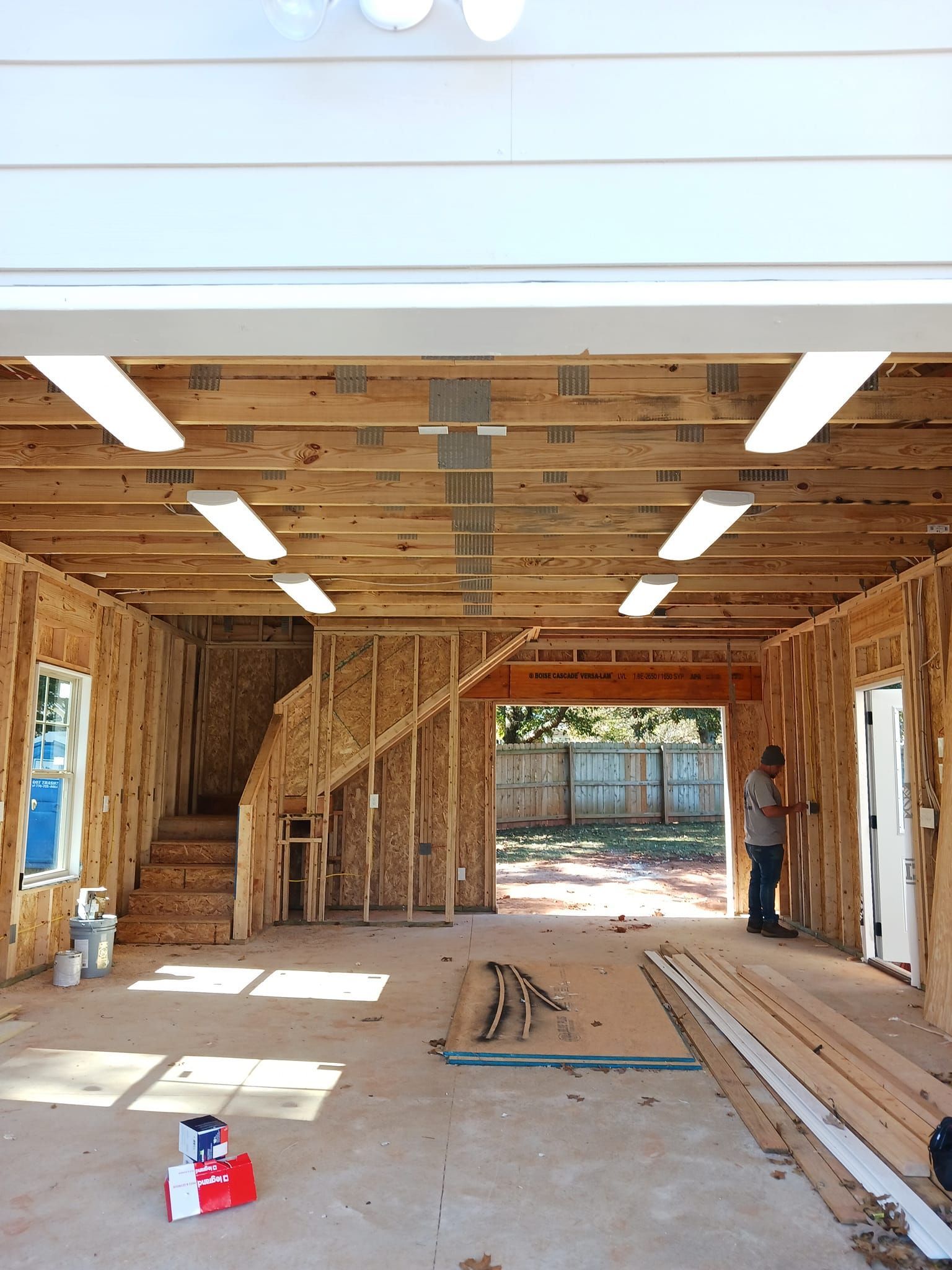 Construction of a garage interior, wood framing, open doorway, fluorescent lights, person.