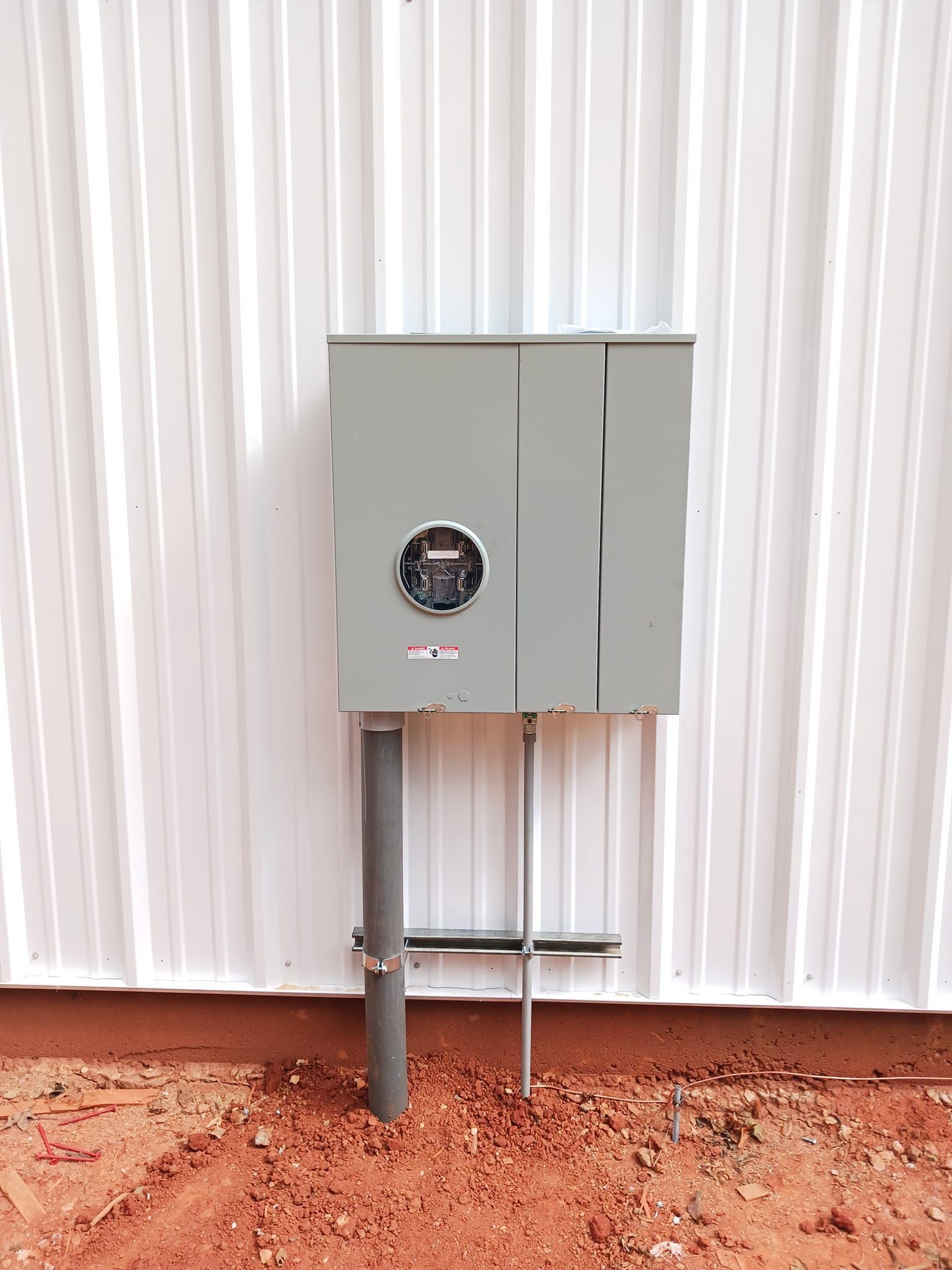 Electrical meter box on a metal building, mounted on a pole with conduit.