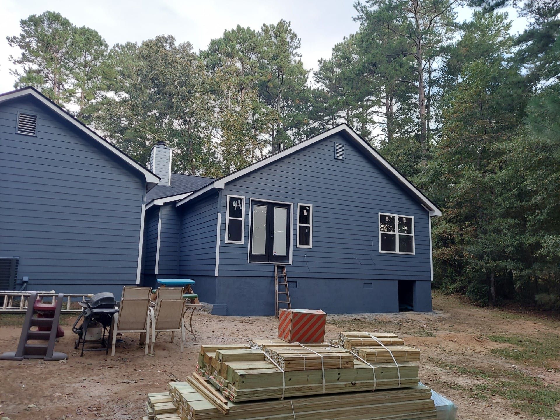 Blue house under construction with materials in the yard, surrounded by trees.