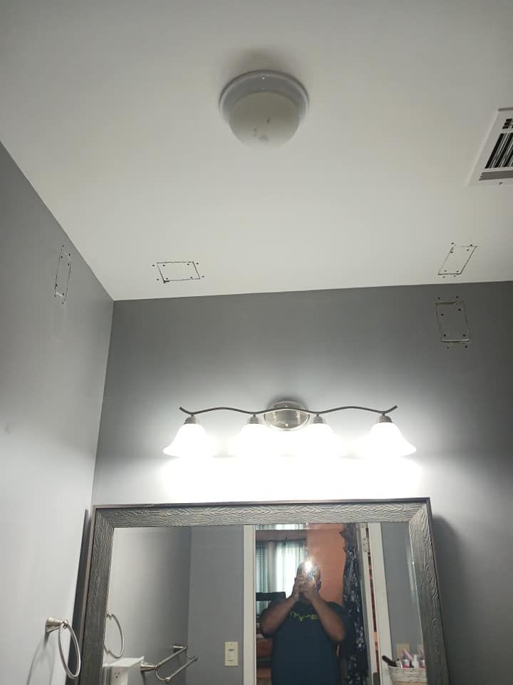 Bathroom ceiling with smoke detector, light fixture, and mirror. Damaged wall around the mirror.