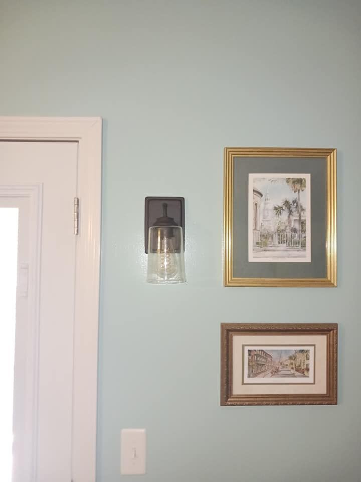 Blue wall with a white door, black sconce, and framed artwork.