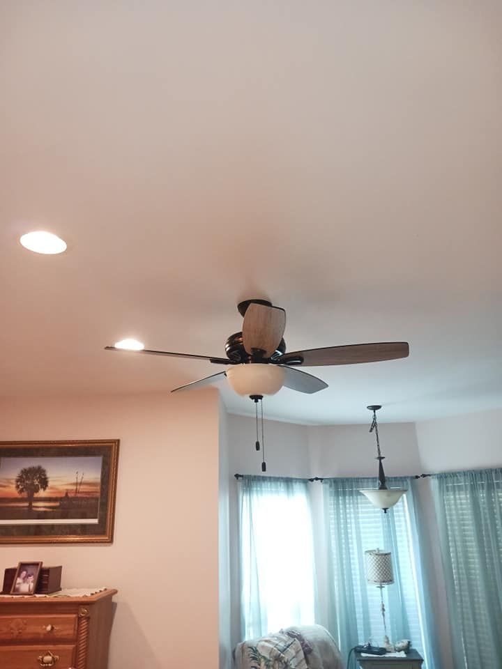 A ceiling fan with lights, recessed lights, painting, and window with curtains in a room.