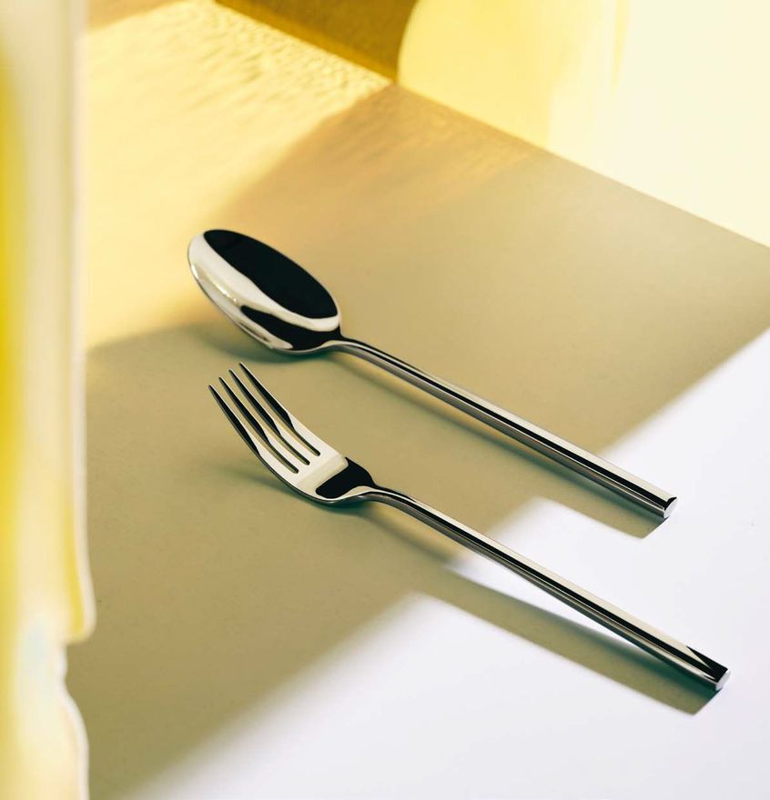 Un cucchiaio e una forchetta su un tavolo illuminato dal sole con ombre morbide.
