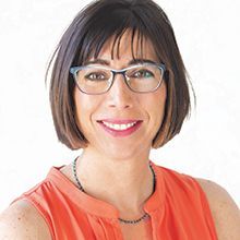 Woman with bobbed hair, glasses, smiling, wearing orange top, looking at the viewer.