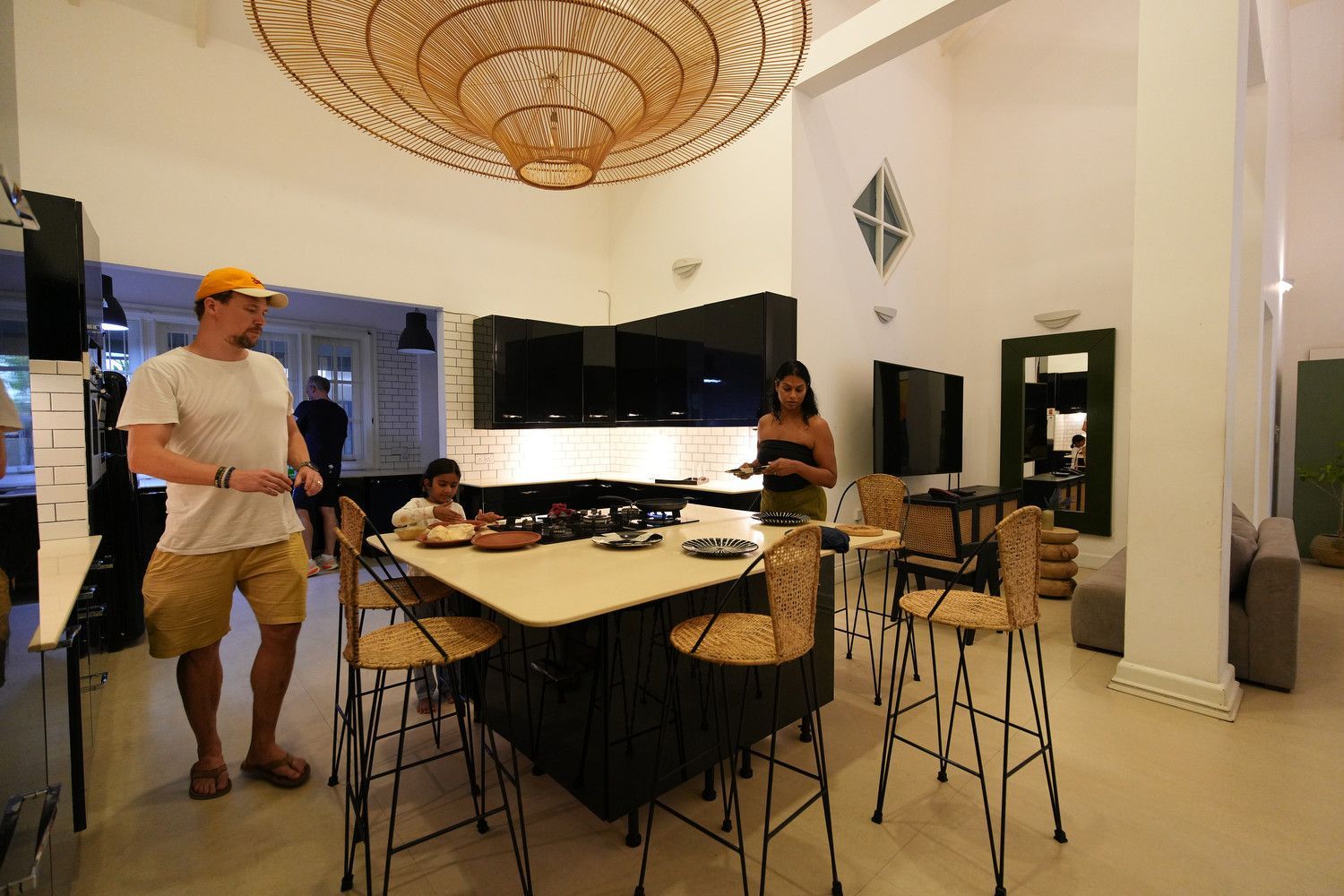People in a modern kitchen with a large island and decorative light fixture.