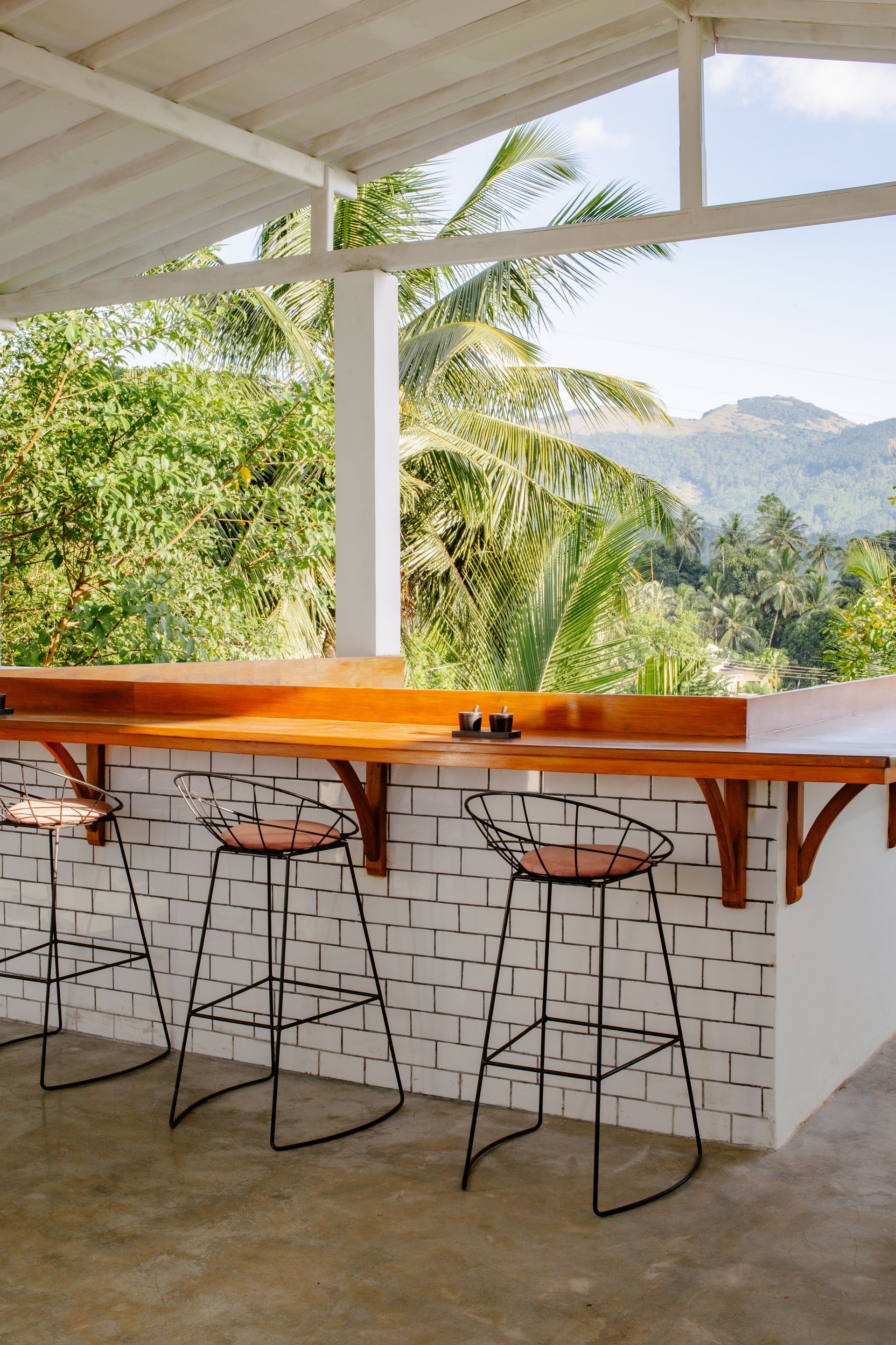 Outdoor bar with stools, wooden counter, and a scenic view of mountains and trees.