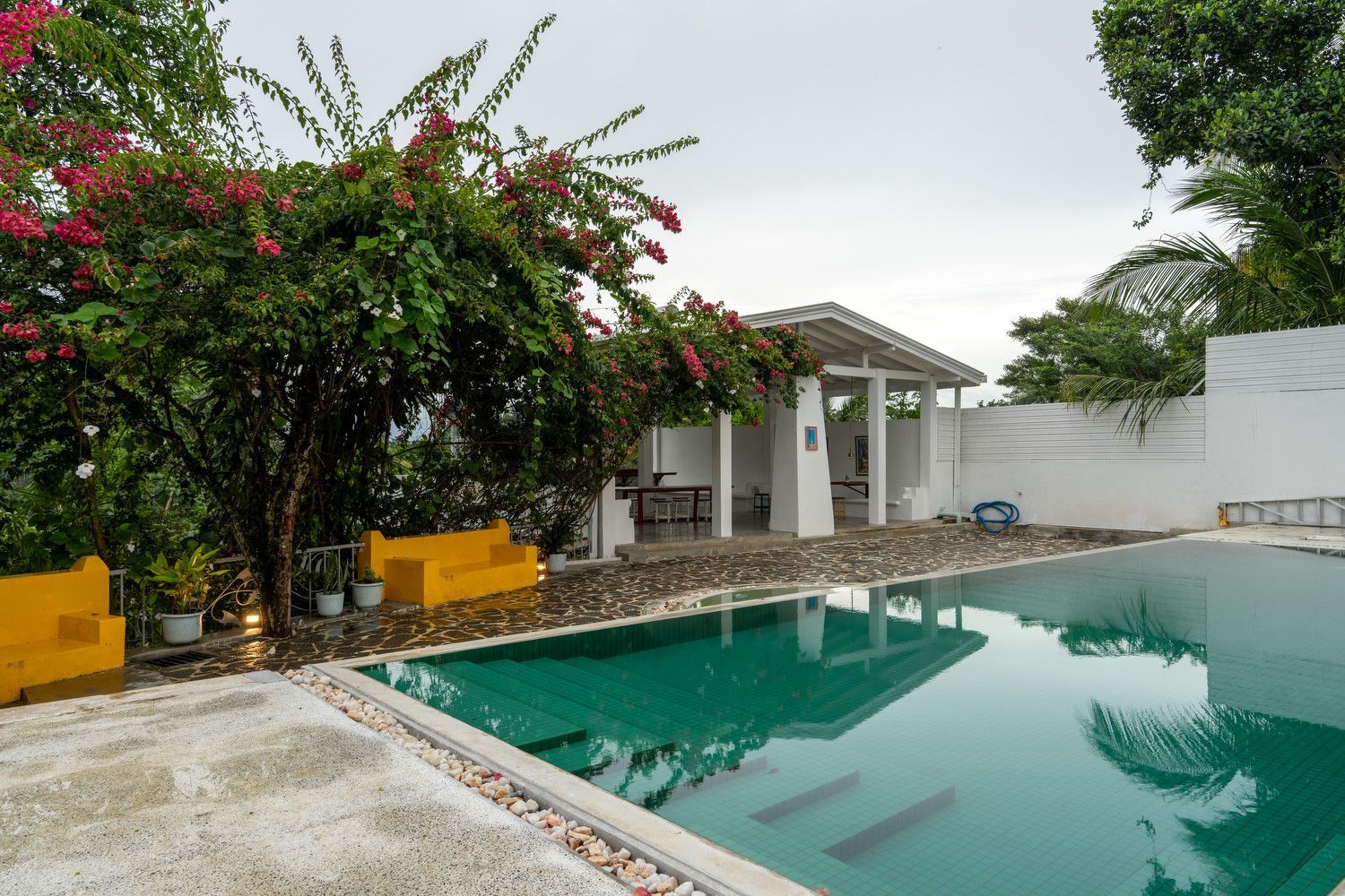 An outdoor swimming pool with turquoise water, adjacent to a patio with yellow seating and a white covered terrace.