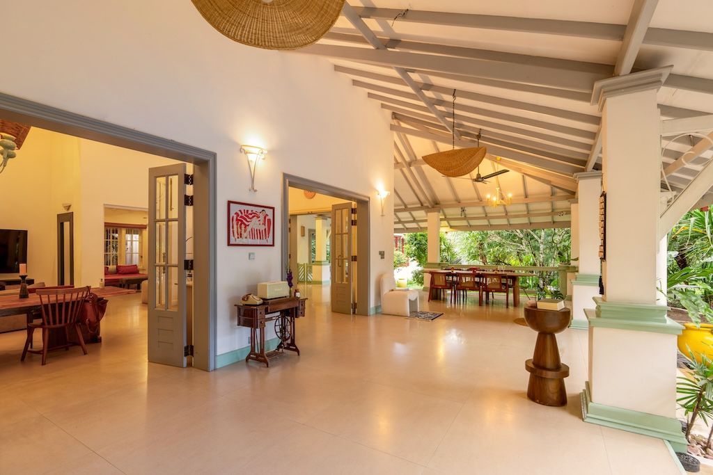 Spacious, open-air veranda with white pillars, overlooking a lush garden and dining area.