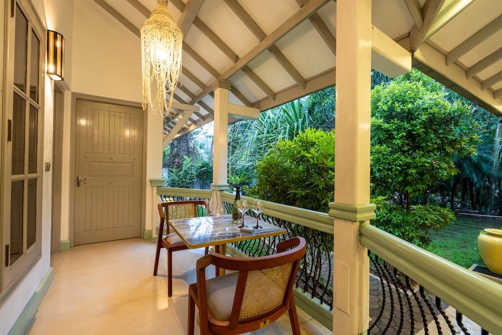 Balcony with a table and chairs, overlooking lush greenery. A decorative light fixture hangs from the ceiling.
