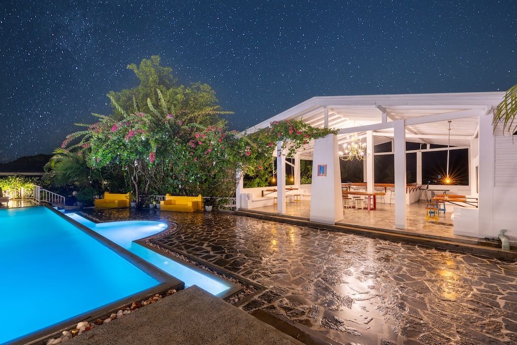 Night view of a swimming pool and a white outdoor dining area under a starry sky.