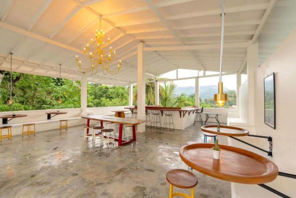 Bright, open-air cafe with white walls, exposed rafters, and wood tables. Overlooks a lush, green landscape.